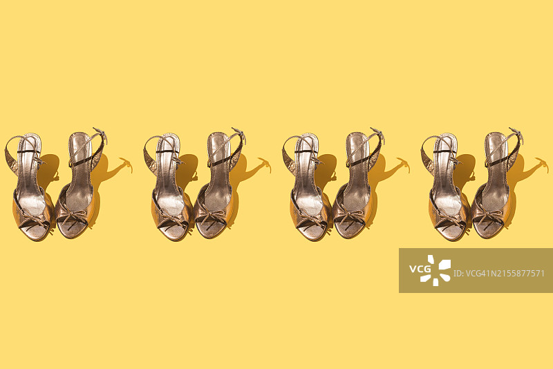 黄色背景上一排金色优雅露趾凉鞋，鞋类、聚会、女性气质概念图片素材
