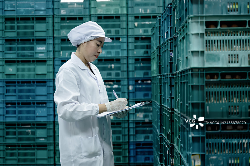 使用供应管理系统支持鸡蛋生产，满足食品需求。食品质检技术员在鸡蛋生产工厂的容器上进行鲜鸡蛋的质量控制。图片素材