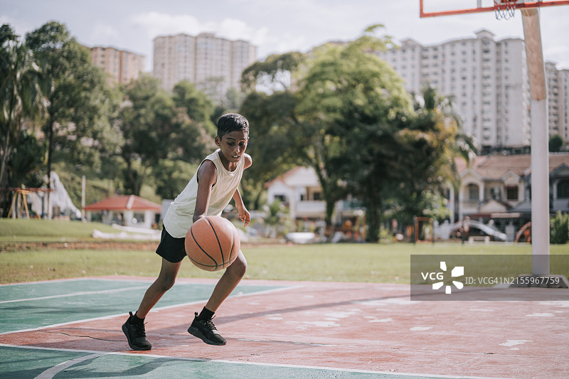 亚洲印度裔男孩在周末早晨的篮球场练习篮球图片素材