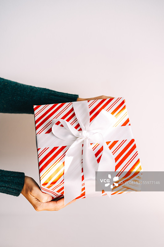 白色背景下，绿色毛衣手中拿着带白色丝带的白色红色圣诞礼物图片素材