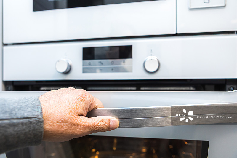 一名男子打开了电烤箱的门，内置烤箱、电器、加热、电力、烹饪概念素材图片素材
