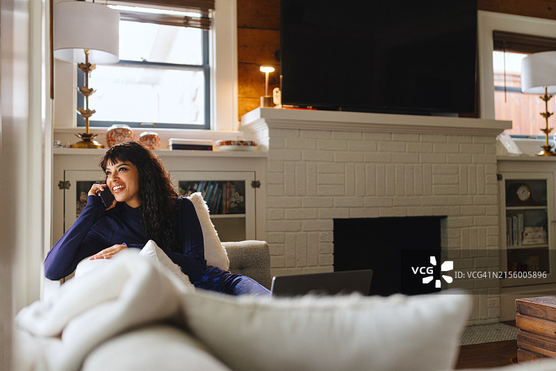 微笑的女人坐在沙发上用智能手机与人交谈图片素材