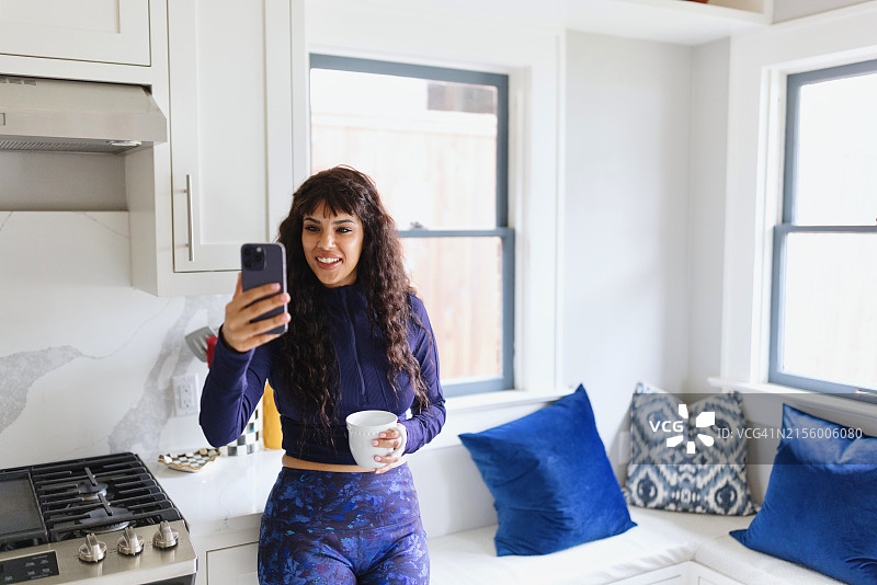 在厨房里用智能手机与人视频通话的微笑女人图片素材
