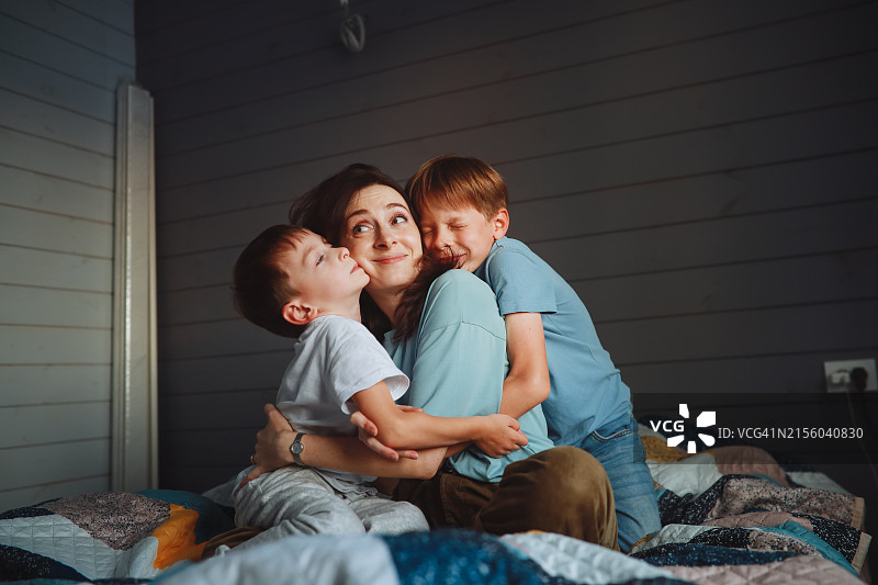 母亲和她的儿子们：孩子们聚集在卧室里疲惫的母亲身边。图片素材
