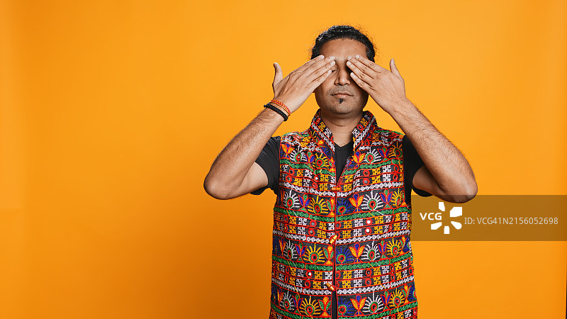 在橙色背景下用手捂住脸的男人图片素材