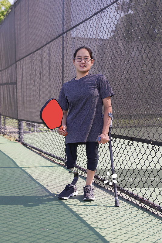 夏天，在户外拿着匹克球拍，穿着休闲服装的中国残疾少女的肖像图片素材