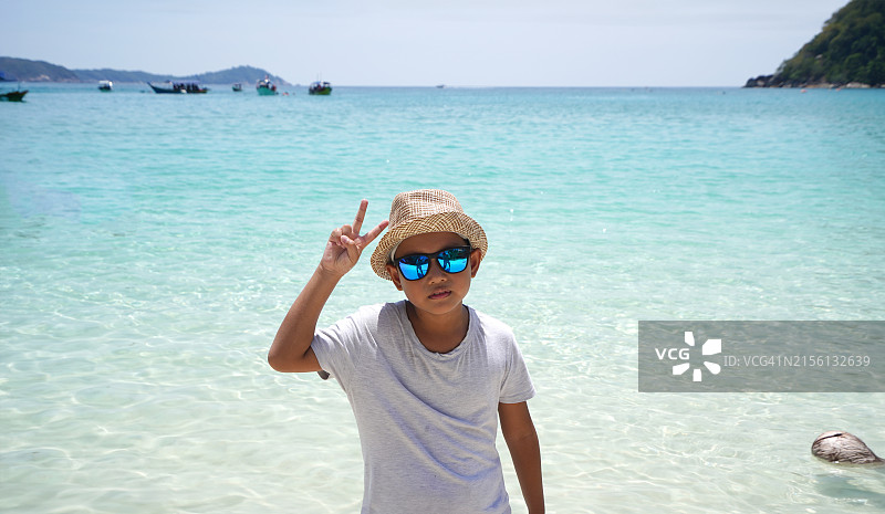 在热带岛屿海滩上做和平手势的亚洲男孩图片素材