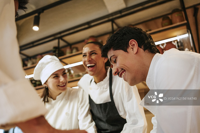 低角度拍摄的年轻男厨师在商业厨房与同事们互动图片素材