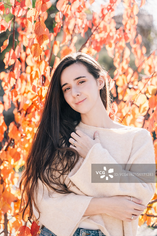 阳光明媚的秋日，橘色秋叶背景上的美丽年轻女人图片素材