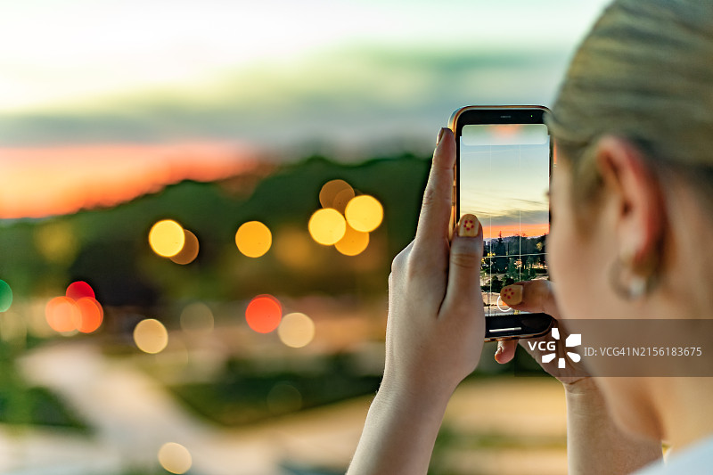 年轻女子用手机拍摄日落时分的城市地平线图片素材