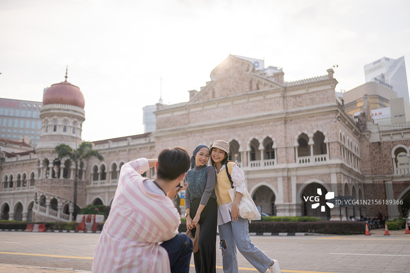 亚洲朋友在标志性城市街道用相机为朋友拍照图片素材