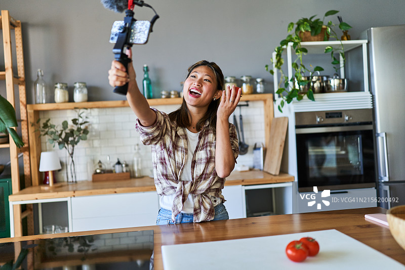 年轻中国女人在网上食谱节目中拍摄自己，手里拿着一个番茄图片素材