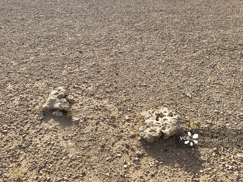 阳光直射下，地面上放置着两块大型不规则形状石头的贫瘠岩石地形图片素材