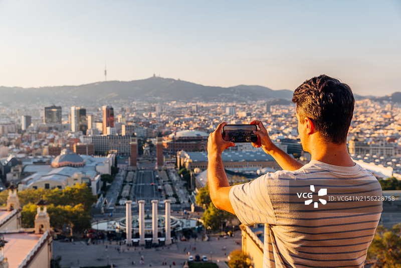 男人在西班牙日落时分用智能手机拍摄巴塞罗那天际线的背影图片素材