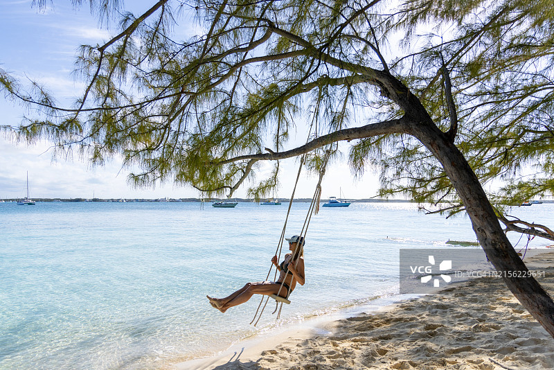 在埃克苏马群岛巴哈马海滩树下的秋千上的女人图片素材