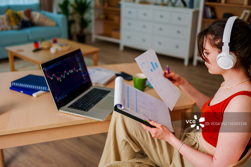 戴着耳机在笔记本电脑上查看比特币或股票交易所价格图表的年轻女商人图片素材