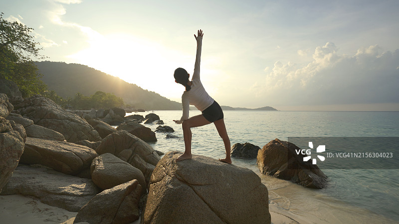 年轻苗条女子在日落时分练习瑜伽，海景图片素材