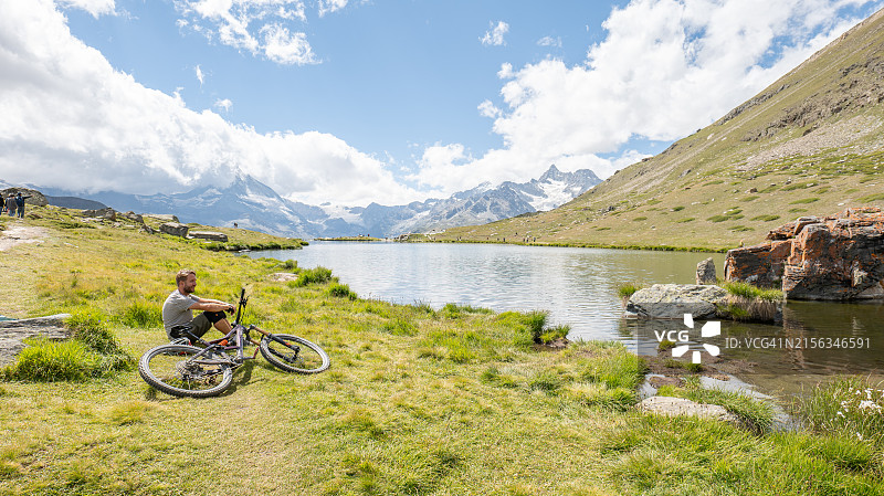 山地自行车手在宁静的阿尔卑斯湖边休息图片素材