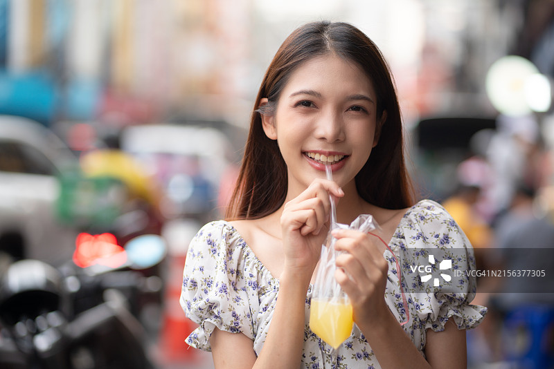 微笑的女人在繁忙街道上喝果汁图片素材