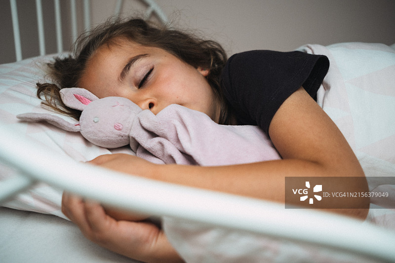 小女孩侧身躺在床上，怀里抱着心爱的玩具兔图片素材