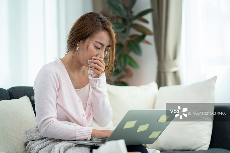 生病中的女人在笔记本电脑前咳嗽图片素材