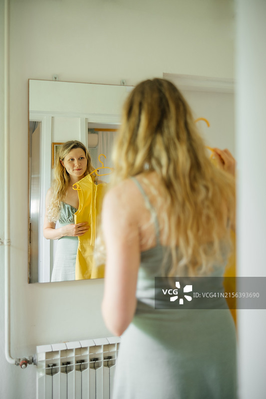 庭院甩卖：女人挑选连衣裙并在镜子中看自己的倒影图片素材