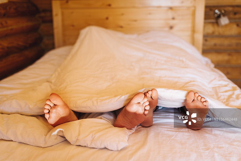 在白色毯子下的情侣的腿，舒适的早晨图片素材