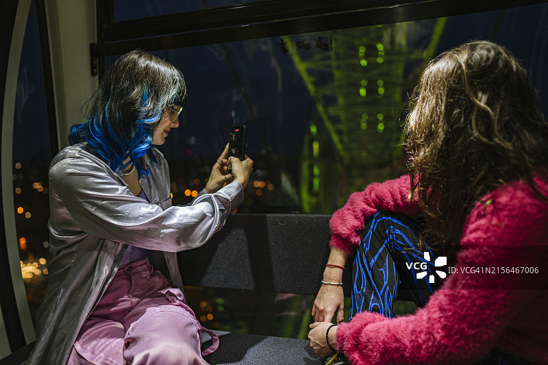 两位女性在摩天轮上眺望窗外，其中一位用手机拍摄视频的场景图片素材