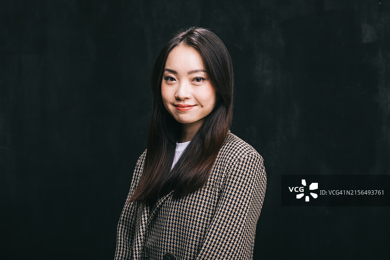 身穿时尚休闲装的亚洲女人自信地站在黑色演播室背景前图片素材