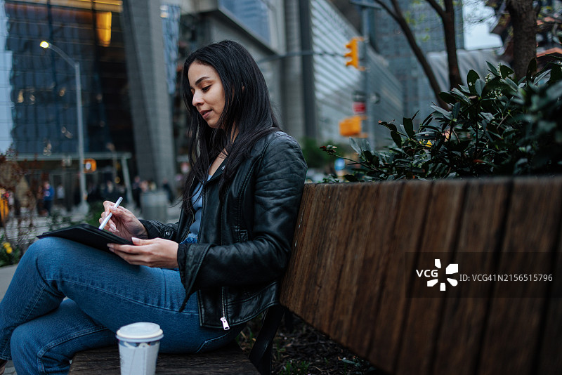 坐在长椅上用平板电脑绘画的可爱女孩图片素材