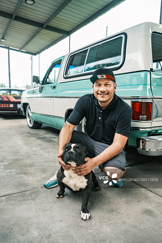中年拉丁裔男性企业主和他的狗在汽车车身喷漆店图片素材