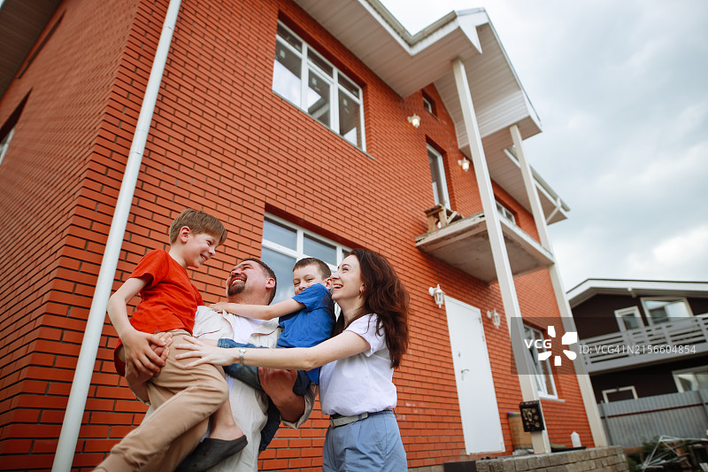 一家人的幸福：父母和两个男孩在新房前拥抱图片素材