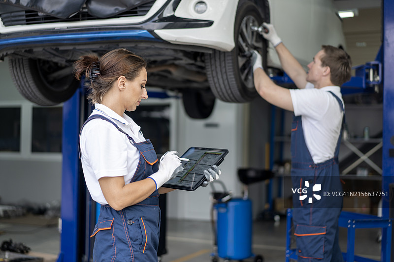 汽车修理厂的主管检查平板电脑，而机械师在后台修理汽车图片素材