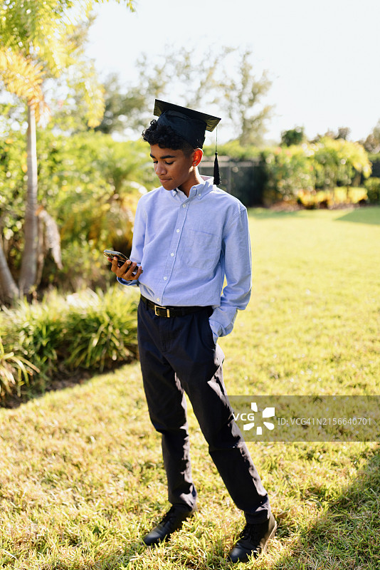 戴着毕业帽看智能手机的现代青少年图片素材