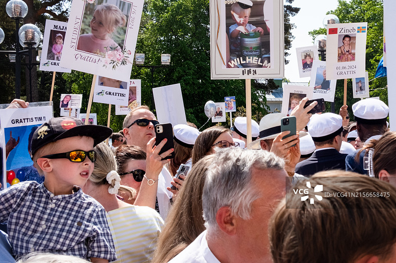 在芬兰奥兰群岛玛丽港奥兰学院毕业典礼上，手持标语和手机庆祝传统北欧节日的友人们图片素材