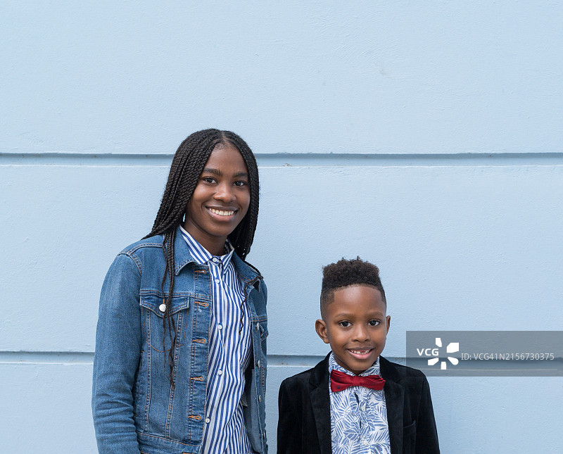 对着蓝色墙壁微笑和摆姿势的少女和她的弟弟图片素材