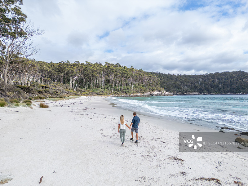 情侣在原始海滩上漫步，背景是森林山丘图片素材