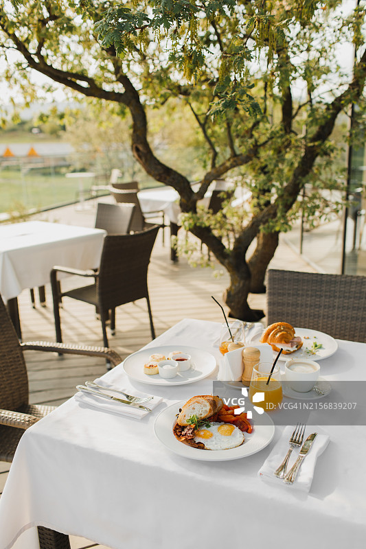 在白色桌布上提供的户外酒店早餐。包括单面煎蛋、橙汁、羊角面包和咖啡图片素材