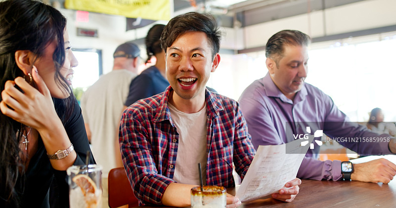 三位顾客在酒吧柜台交谈，其中一人手持菜单 - 白天图片素材