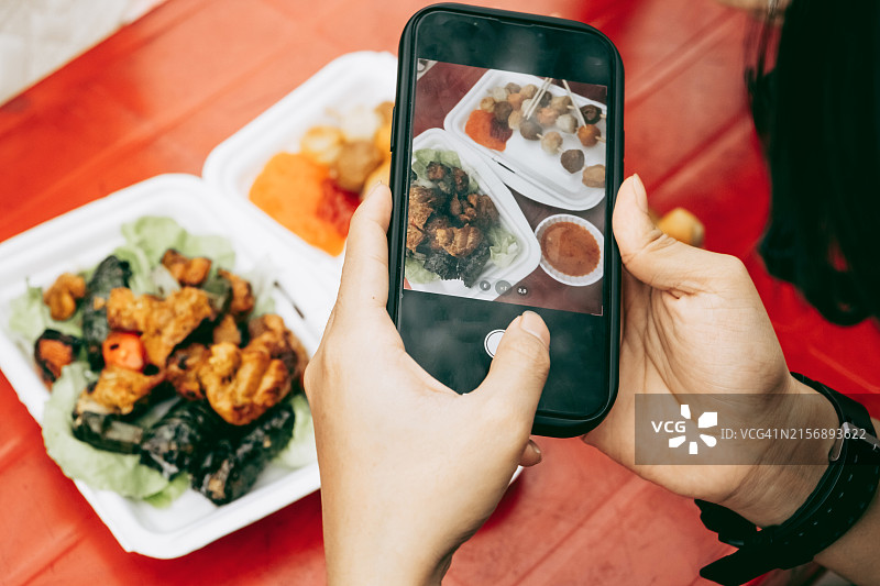手持智能手机拍摄红色桌子上的亚洲外卖图片素材