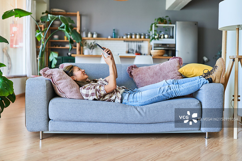在现代住宅内沙发上使用手机的年轻亚洲女性图片素材