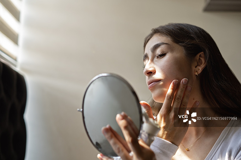 年轻女子在晨间护理时往脸上涂润肤霜图片素材
