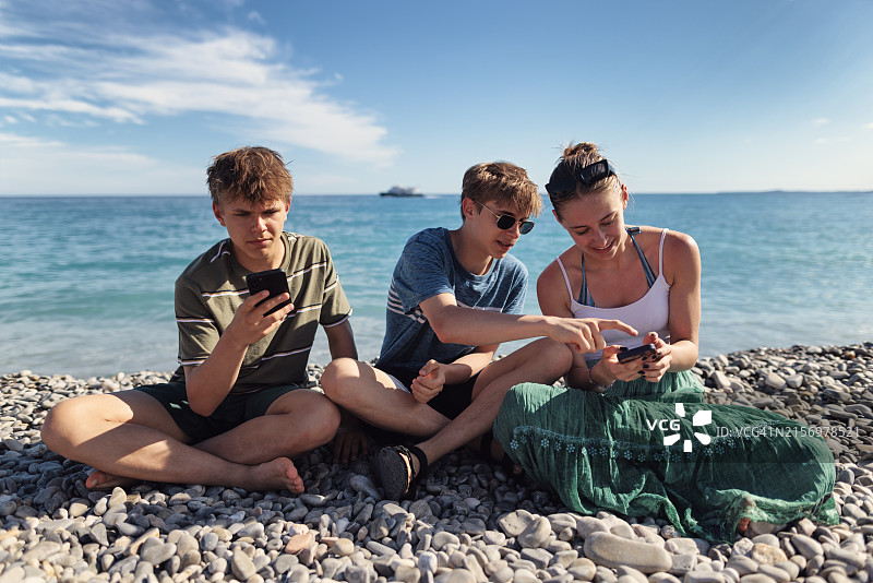 在法国尼斯卵石滩上使用手机的青少年图片素材