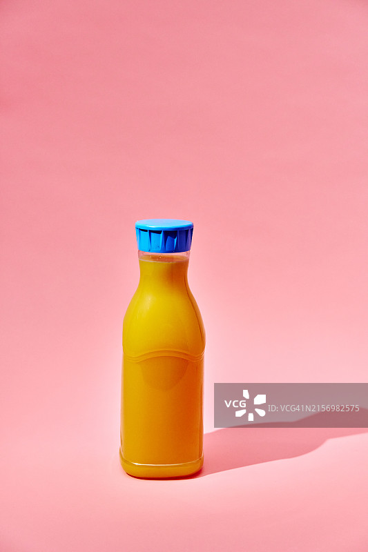 粉色背景上的再生PET塑料瓶装橙汁图片素材