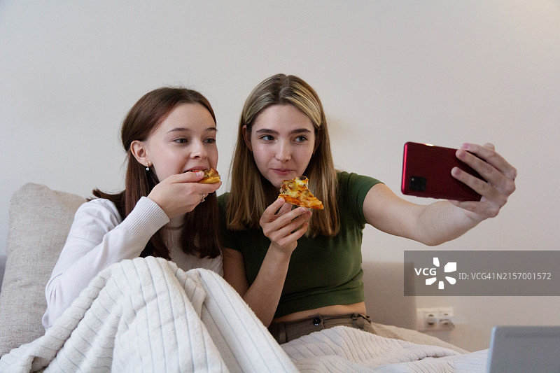 两个朋友在床上吃披萨自拍图片素材