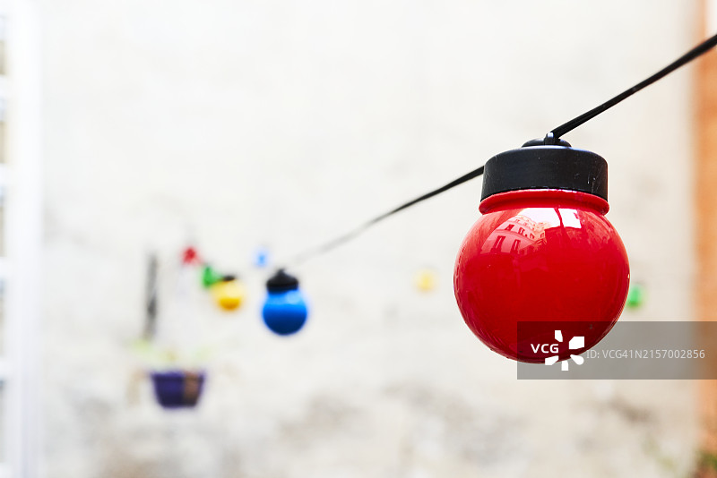 一排彩色灯泡悬挂在建筑物外的电缆上（侧视图）图片素材