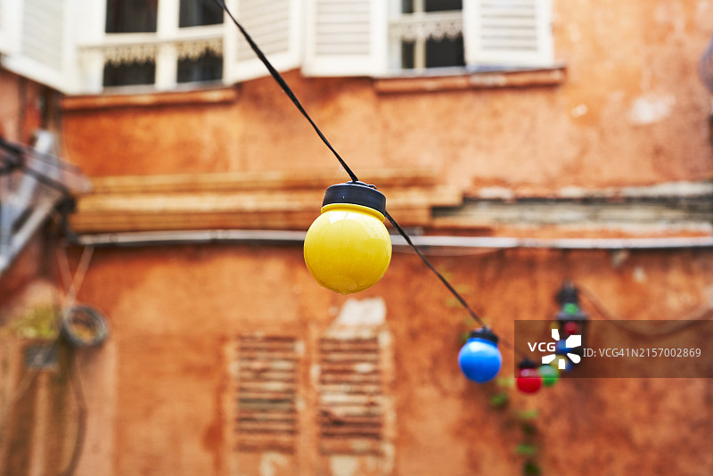 一排彩色灯泡悬挂在建筑物外的电缆上（侧视图）图片素材
