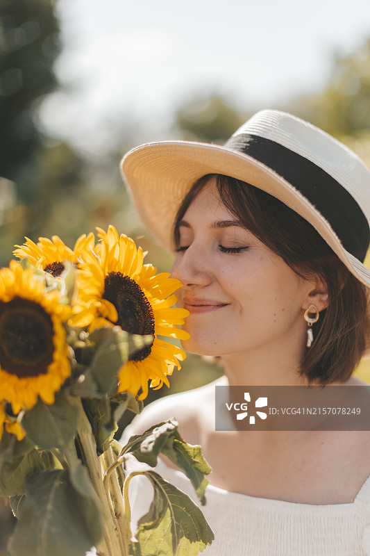 微笑的戴帽子女子在田野里闻向日葵图片素材