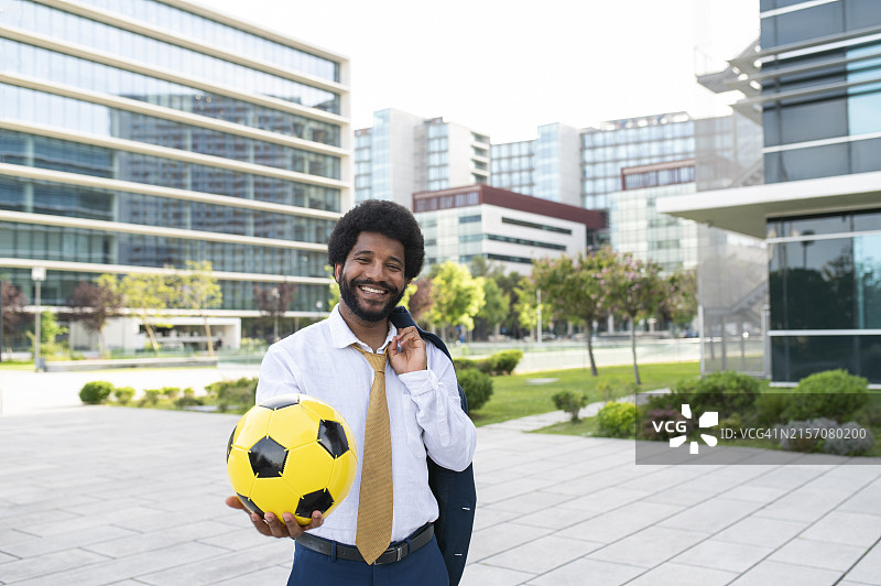 微笑的商人在办公园区拿着黄色足球图片素材