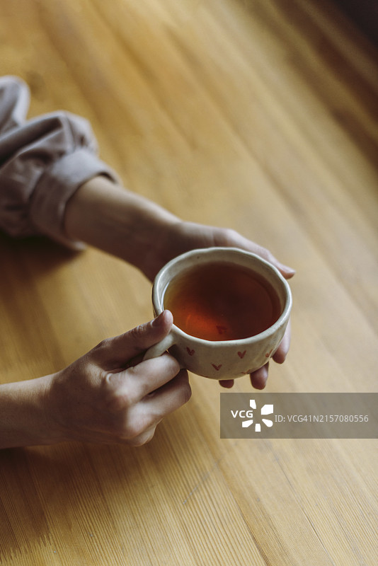 女子在桌旁手捧茶杯图片素材